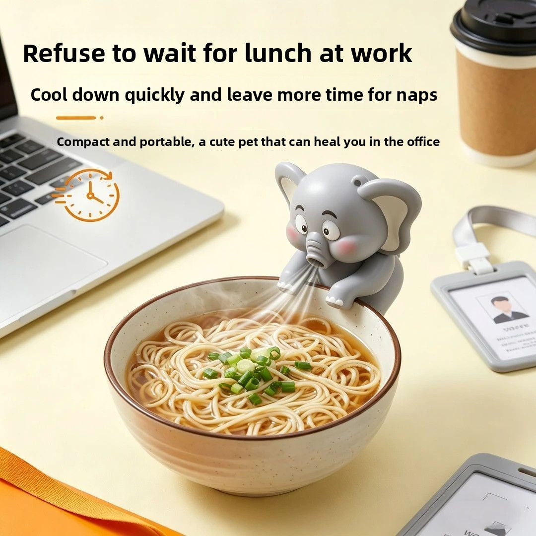 A novelty pet product shown in a styled office desk scene: a small gray elephant-shaped straw holder perched over a bowl of noodles, with text at the top describing cooling down quickly and napping. The scene includes a laptop, coffee cup, ID badge, and part of another device, so this is Lifestyle rather than Product/Packaging.